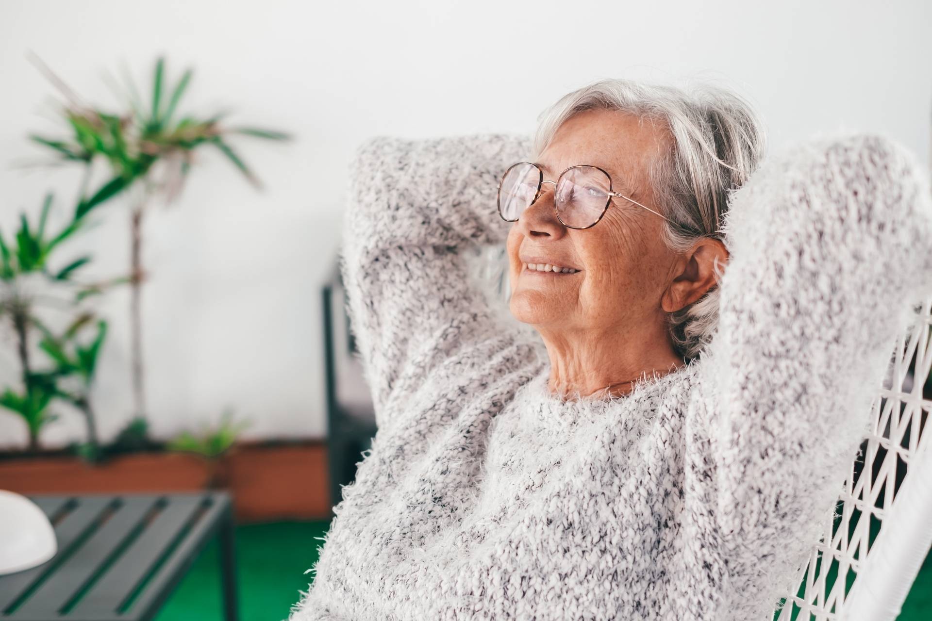 Smiling older woman with glasses relaxing in a cozy chair at home.